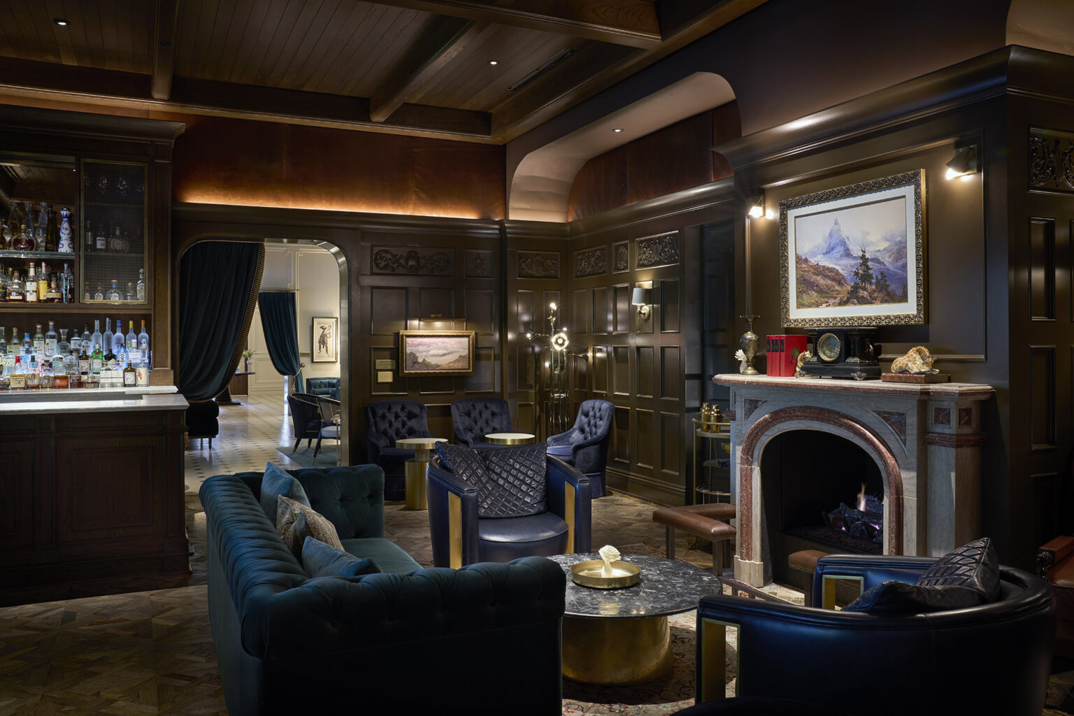 Isabelle's bar at Hôtel Swexan, a warmly lit lounge with a fireplace, full back bar, and deep-toned seating — the kind of room that sells wine at 3pm as readily as midnight.